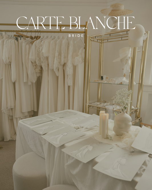 Interior of Carte Blanche Bride Melbourne showroom featuring wedding dress sketches on a table and a rack of silk made-to-order gowns, representing a calm start to the bridal journey.