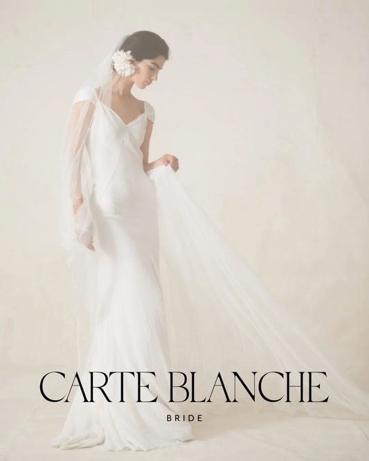 Elegant bride wearing the Cortana Elina wedding dress with a deep V-neckline and cap sleeves, styled with a floral hairpiece and long veil at Carte Blanche Bride.