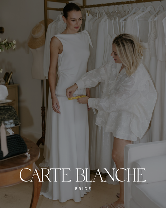 Woman in a tailored blazer carefully browsing through high-end, sustainable wedding dresses on a rack at the Carte Blanche Bride bridal boutique, showcasing slow fashion luxury.