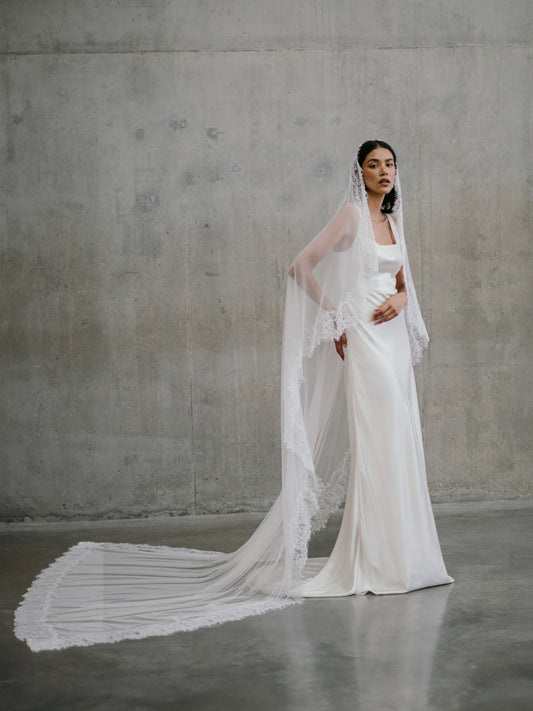 Full-length view of the Clara silk gown paired with a long cathedral-length lace-edged veil extending behind.