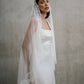 Close-up portrait of model wearing the Clara gown styled with a delicate scalloped lace mantilla veil over her head.