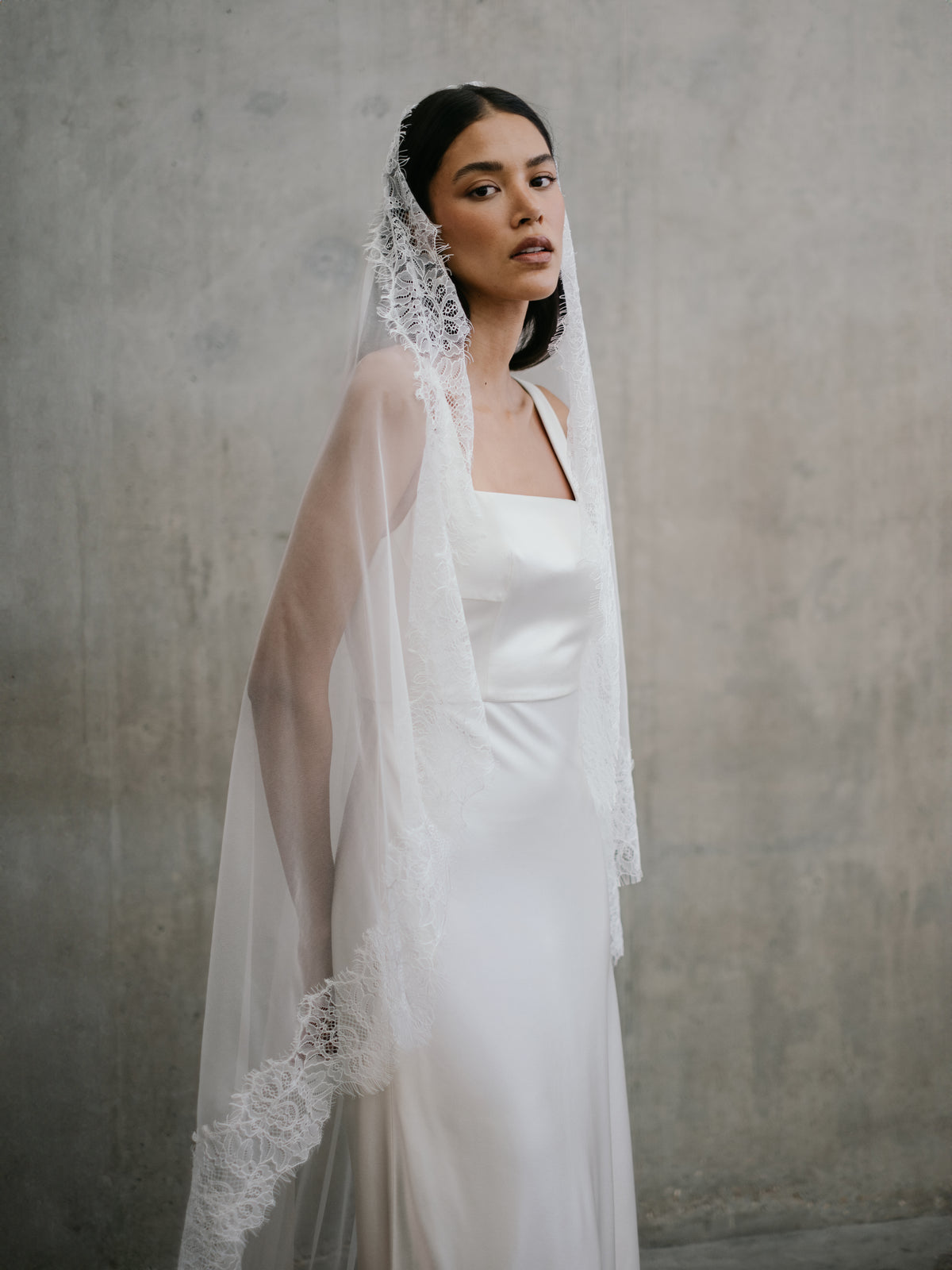 Close-up portrait of model wearing the Clara gown styled with a delicate scalloped lace mantilla veil over her head.
