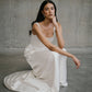 Seated floor shot displaying the pooled silk train and low-back detail of the Clara wedding dress.