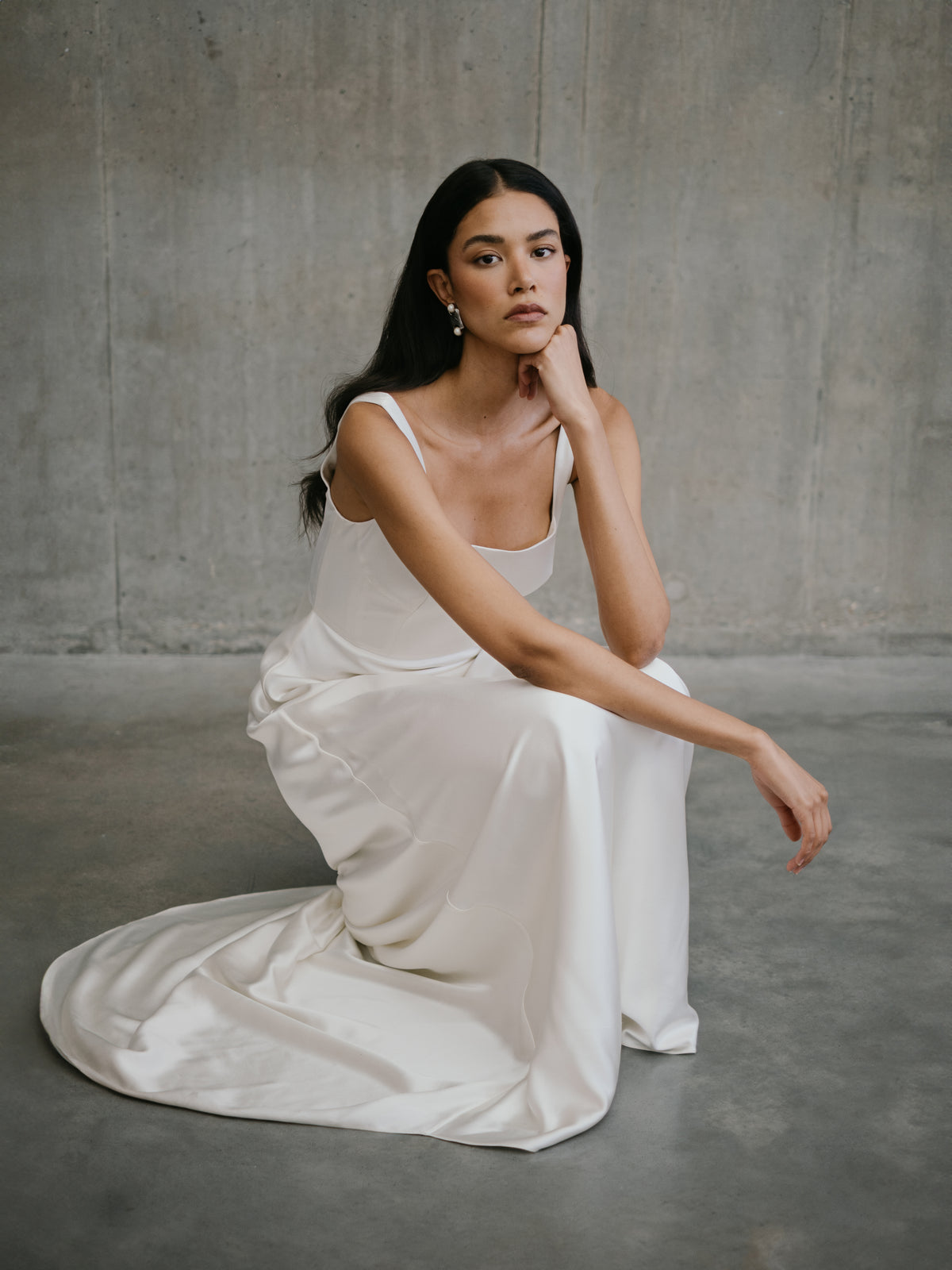 Seated floor shot displaying the pooled silk train and low-back detail of the Clara wedding dress.