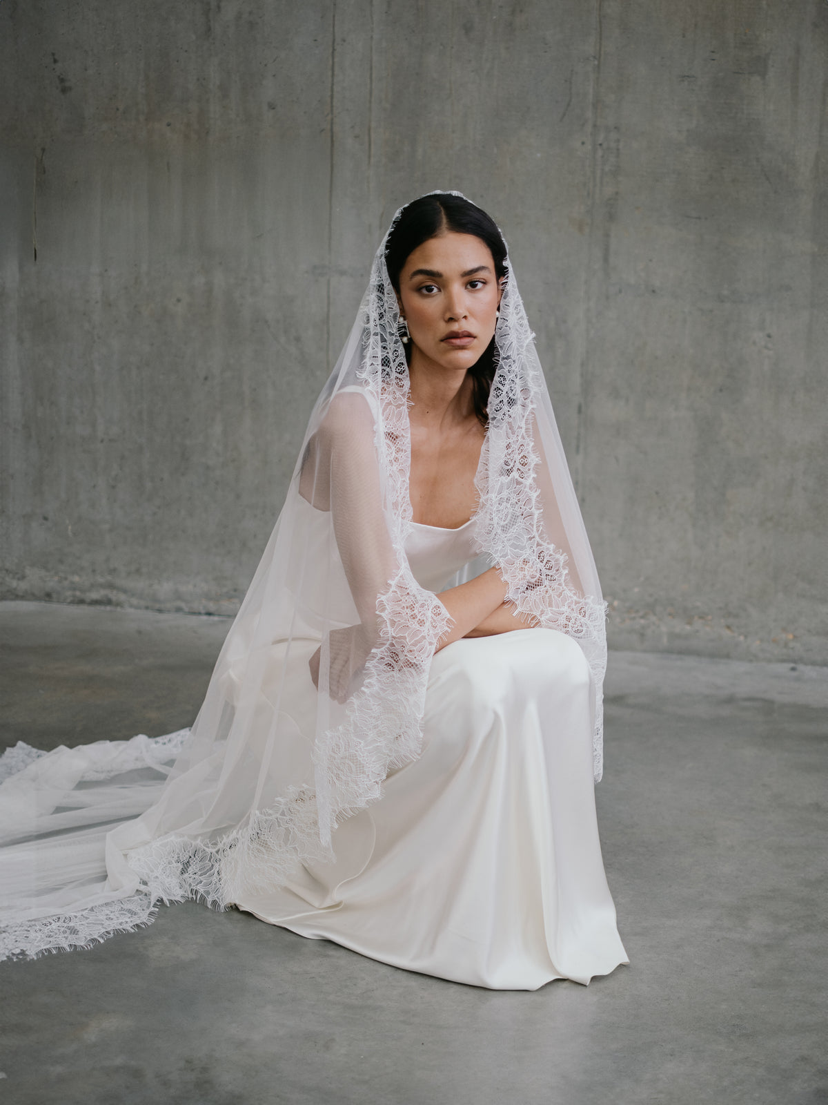 Seated portrait of model wearing the silk Clara wedding dress and lace-trimmed mantilla veil.