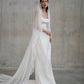 Side-angle standing portrait of the Clara wedding gown and long draped lace veil at Carte Blanche Bride.