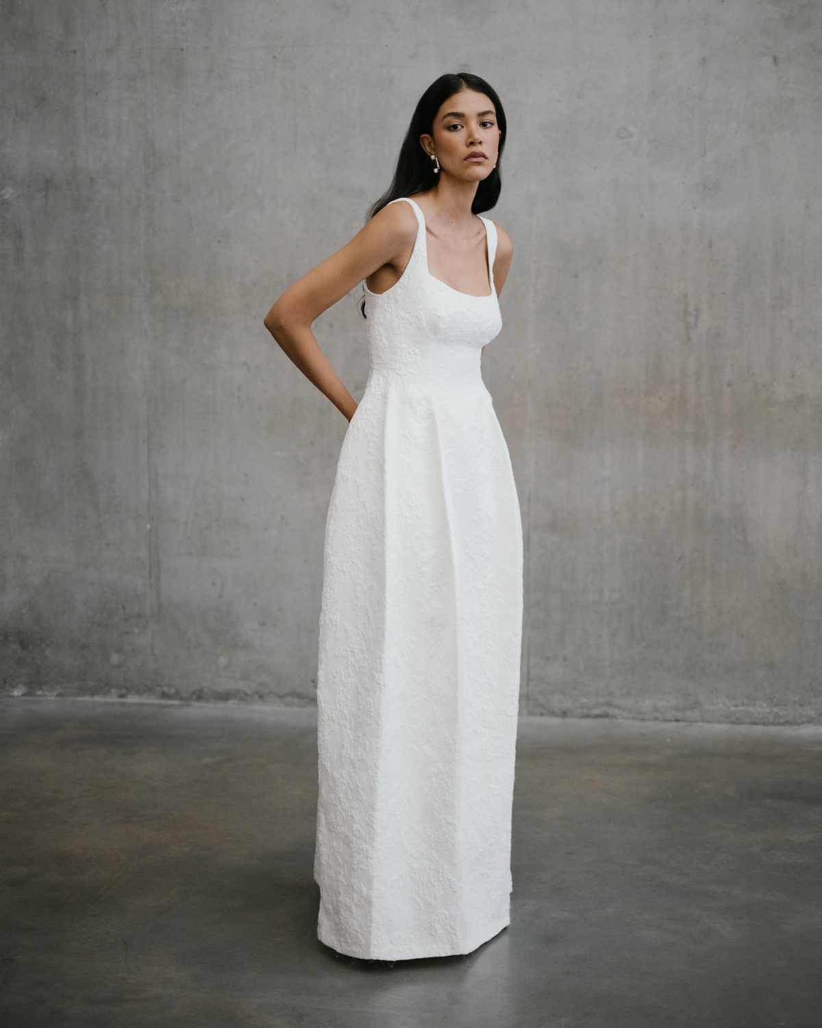 Standing full-length profile showing the elegant A-line fall and inverted pleats of the Thora gown by Unbridled Studio.